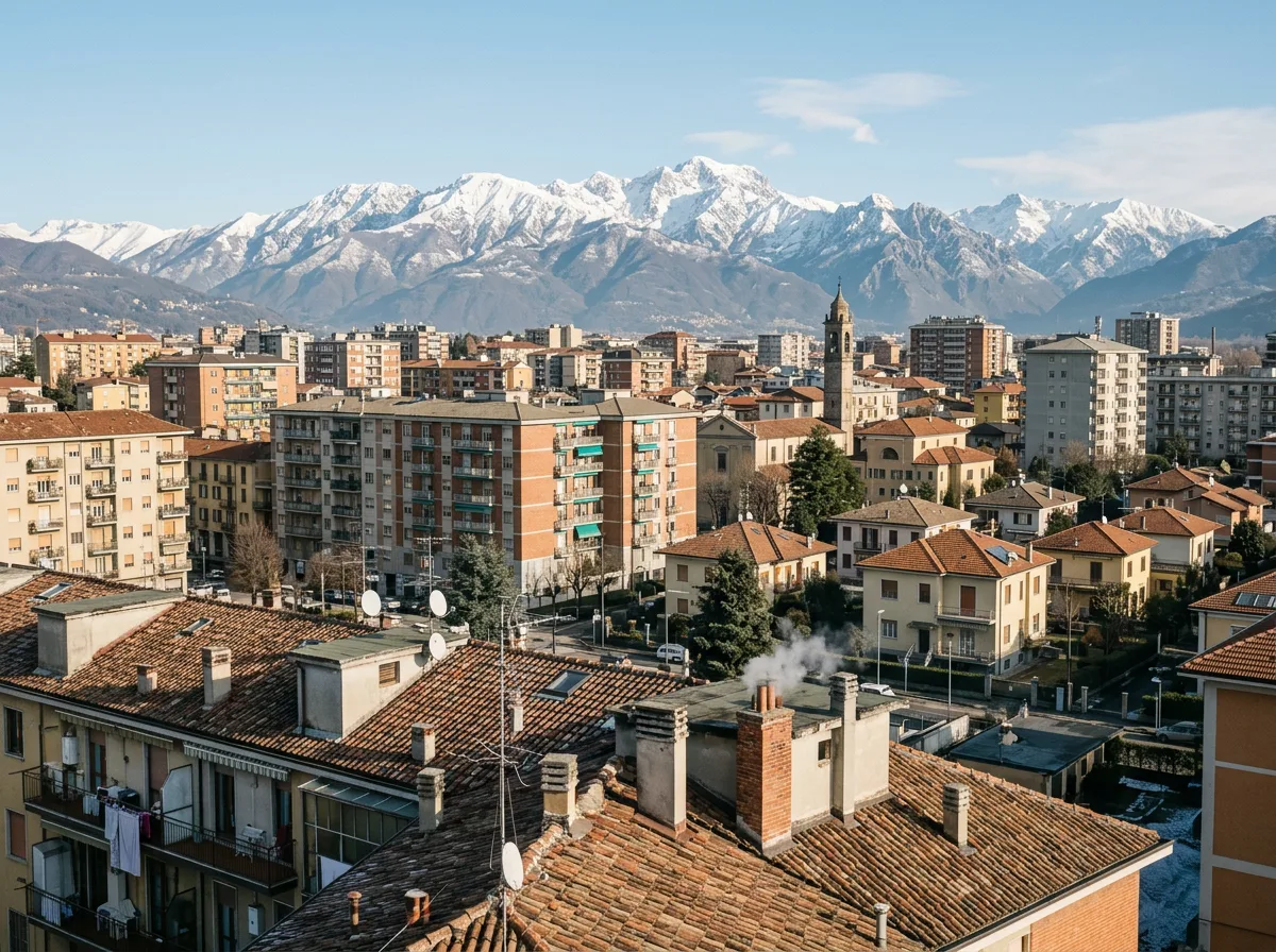 Skyline residenziale di una città lombarda con condomini e villette, tetti e comignoli in primo piano e le montagne sullo sfondo